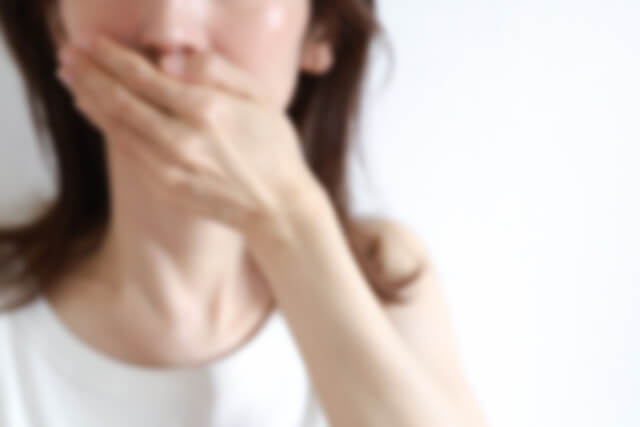 白い服を着て口を押さえる女性