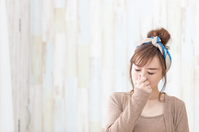 鼻をつまむ茶色い服を着た女性