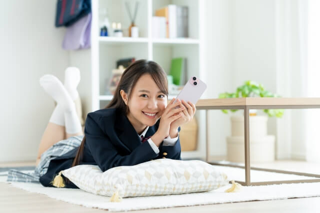 スマートフォンを持って寝そべる女子高生