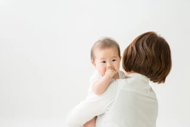 ママに抱かれて指を咥えている赤ちゃん