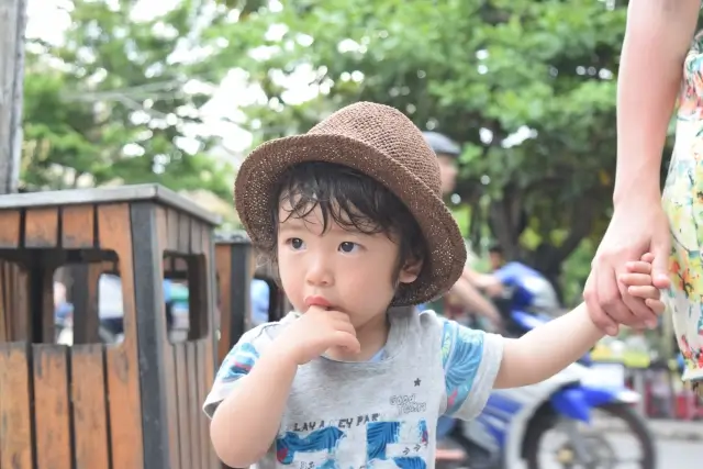 母親に手を引かれながら指しゃぶりをする男の子